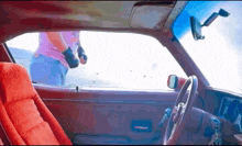 a man in a pink shirt is standing in a car looking out the window