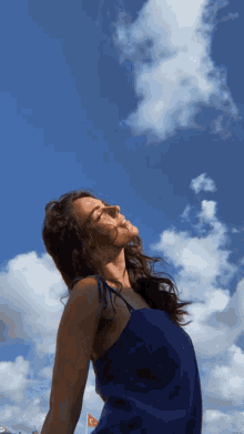 a woman in a blue dress looks up at a blue sky with white clouds