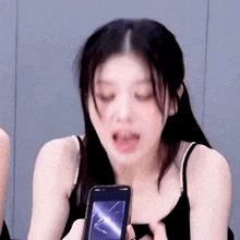 a woman in a black tank top is holding a cell phone in her hand .