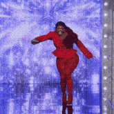 a woman in a red suit is dancing in front of a blue curtain