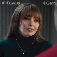 a woman wearing a green turtleneck and a necklace says " okay "