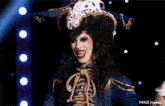a drag queen is holding a rope and smiling in front of a dark background that says taycs tumblr