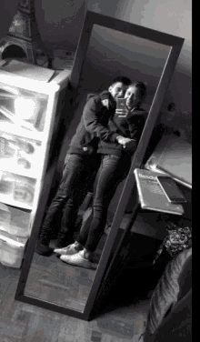 a black and white photo of a man and woman taking a selfie in front of a full length mirror