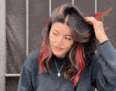 a woman with red streaks in her hair is wearing a black sweater and necklace .