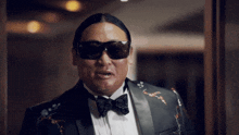 a man wearing sunglasses and a tuxedo has a bow tie