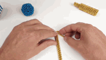 a person is playing with gold and blue beads on a table