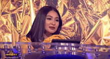 a woman in a yellow jacket is sitting in front of a gold foil background .