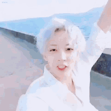 a young man with white hair is taking a selfie on the beach .