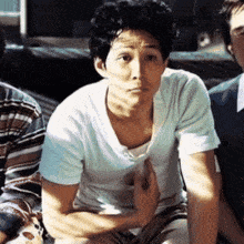 a man in a white t-shirt is sitting with his hands on his knees