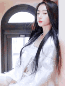 a woman with long black hair is leaning against a wall and wearing a white jacket