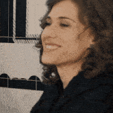 a woman in a black jacket is smiling in front of a black and white tiled wall