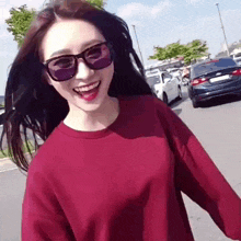 a woman wearing sunglasses and a red shirt smiles while walking down the street