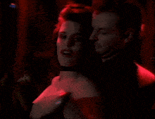 a man and woman are dancing in a dark room with red lights behind them
