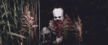 pennywise the clown is holding a bloody knife in a field .