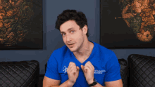 a man wearing a blue shirt that says ' mike ' on it sits on a couch