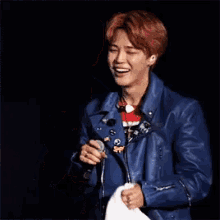 a man in a blue leather jacket is holding a white towel in his hands and smiling .