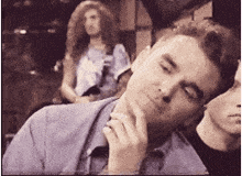 a man in a blue shirt is thinking with his hand on his chin .