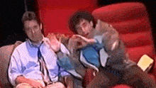 two men are sitting next to each other in a red chair .