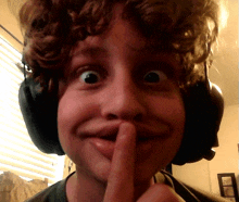 a young boy wearing headphones holds his finger to his lips