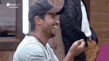 a man wearing a baseball cap is laughing while sitting in front of a wooden building .