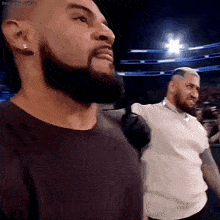 a man with a beard is standing next to another man in a wrestling ring .