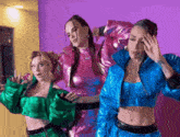 three women are standing next to each other on a purple background wearing metallic outfits .
