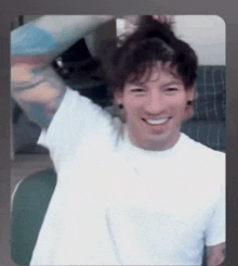 a man in a white shirt is smiling and holding his hair in a bun .