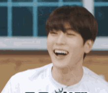 a young man is laughing with his mouth open and wearing a white shirt .