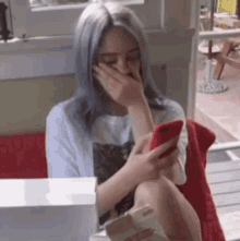 a woman with blue hair is covering her mouth while looking at her phone .