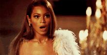 a woman in a feathered dress is standing in front of a chandelier and making a surprised face .