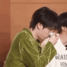 a man in a green shirt is drinking from a glass while sitting next to another man .
