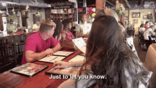 a group of people are sitting at a table in a restaurant with a sign that says just to let you know