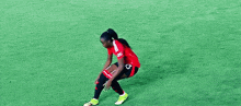 a female soccer player wearing a red jersey and black shorts is kneeling on the field .