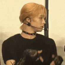 a man with blonde hair is wearing a choker and a microphone around his neck