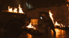 a man is laying on the ground in front of a car on fire
