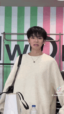 a young man in a white sweater is making a funny face while holding a bag and a bottle of water .