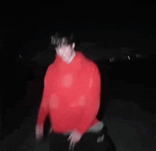 a person in a red hoodie and black pants is jumping in the air at night .