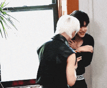 a man and a woman are hugging in front of a window and the woman is wearing a moschino belt
