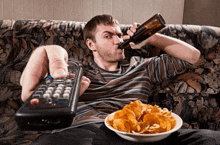 a man sitting on a couch holding a remote control and a bowl of chips