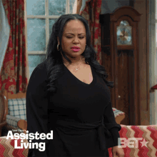 a woman in a black dress is standing in front of a couch and a poster for assisted living