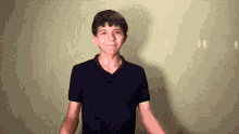 a young man in a black shirt is standing in front of a wall .