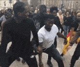 a group of people are dancing on a street with one wearing a white shirt with adidas on the bottom