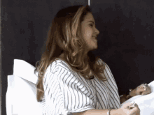 a woman in a striped shirt is sitting on a bed and smiling