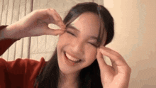 a woman is smiling and making a heart shape with her hands on her face .