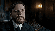 a man with a beard and mustache is wearing a suit and tie and looking at the camera .