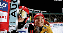 two skiers are posing for a picture with one wearing a helmet that says augment on it