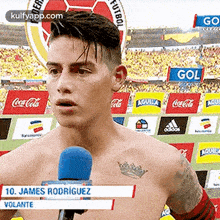 a shirtless soccer player is talking into a microphone while standing in front of a crowd .