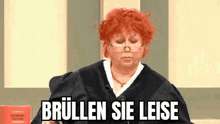a woman with red hair is wearing glasses and a judge 's robe and is sitting in a courtroom .