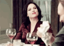 a woman is sitting at a table with a man holding a napkin and a glass of wine .