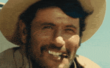 a man with a hat and a beard is smiling and smoking a cigar